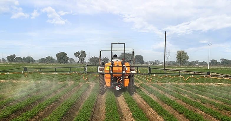 Ein Traktor mit Spritzgestänge bei der Flächenbehandlung eines Feldes.