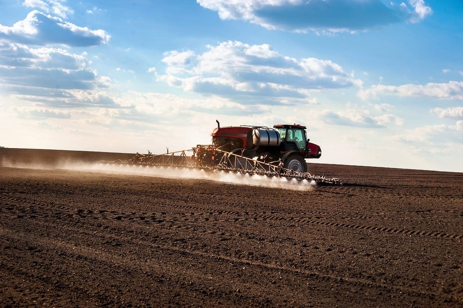 Een tractor met spuitboom die vlakdekkend over een veld spuit.