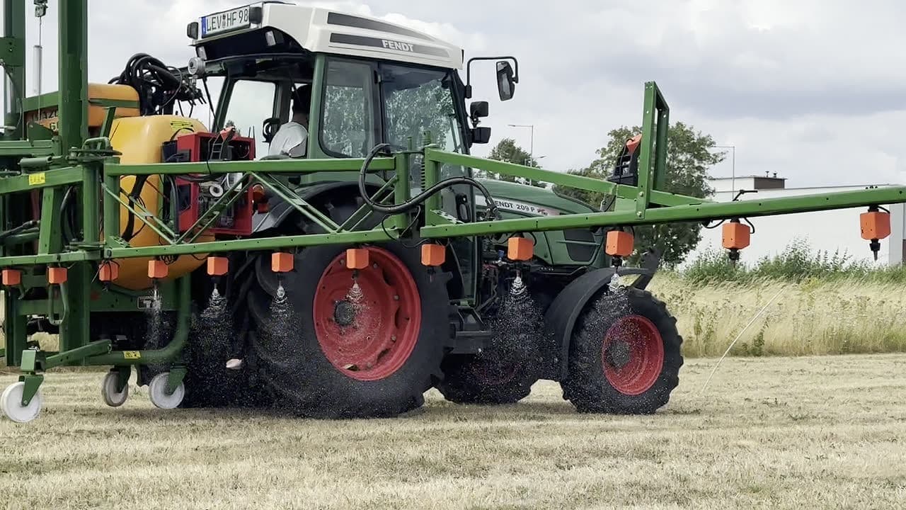 Une rampe de pulvérisation portée par un tracteur et équipée de WeSee, dont les vannes de buses individuelles pulvérisent par jets courts et ciblés au-dessus d'un champ.