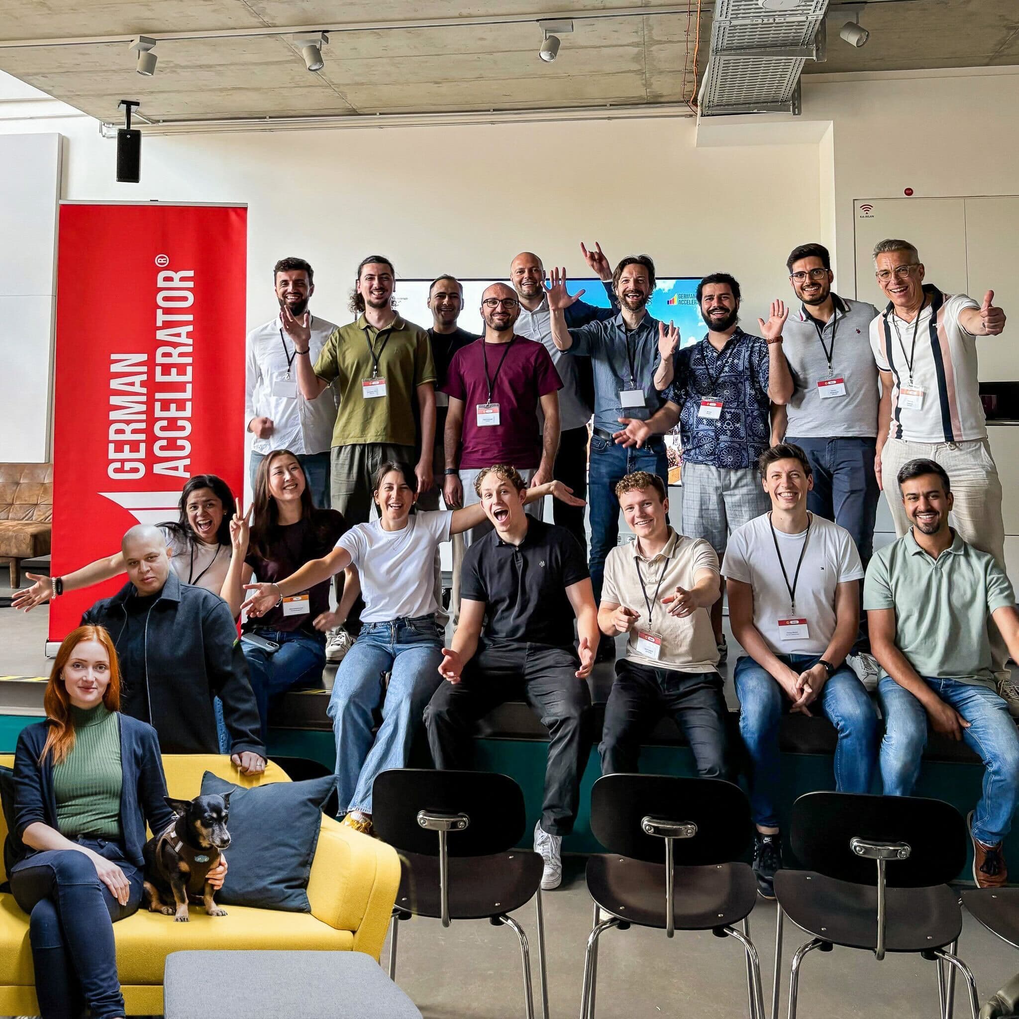 Large group of founders posing under a German Accelerator banner indoors, several with hands raised.